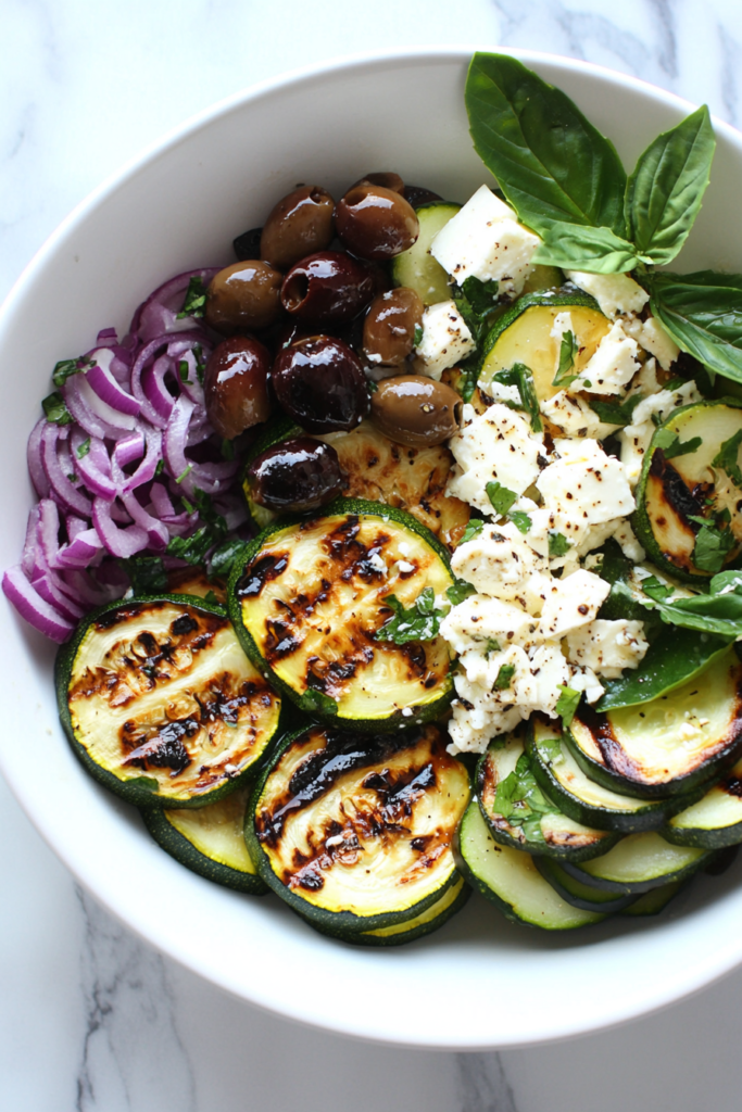 this image shows A flavorful Grilled Zucchini Greek Salad with charred zucchini slices, caramelized onions, and kalamata olives, offering a smoky and tangy taste, beautifully arranged on a marble plate.