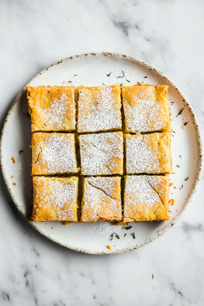 this image shows Keto-friendly zucchini bars served on a white round plate, cut into squares, featuring a smooth layer of cream cheese and caramel sauce for a rich, indulgent dessert