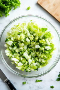 This image shows a fresh layer of crisp, green lettuce being evenly arranged in the base of a glass bowl, preparing the first layer of the layered salad.