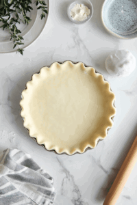 This image shows the dough being carefully pressed into a tart tin, forming a smooth, even crust with fluted edges.