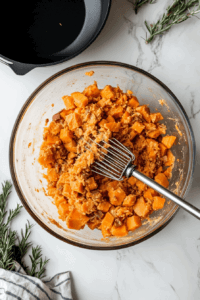 This image shows a large mixing bowl with a hand masher or stand mixer, turning the boiled sweet potatoes into a smooth and creamy consistency.