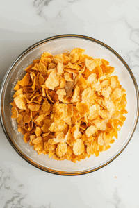 this image shows Crushed cornflakes being added to a seasoned flour mixture, enhancing the crunchiness of the tofu coating.