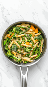 this image shows Fresh basil leaves, chopped parsley, and lemon zest being stirred into the pasta and vegetable mixture, adding brightness to the Vegan Pasta Primavera.