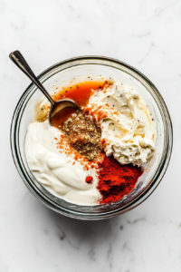 This image shows a bowl filled with mayonnaise, Creole mustard, horseradish, garlic, Cajun seasoning, and pickle juice being mixed to create a tangy remoulade sauce for the Po'Boy sandwich.