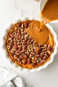 This image shows the pecan filling being poured over the baked sweet potato layer in the pie crust.