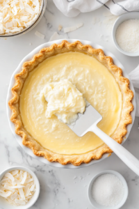 This image shows the smooth and creamy coconut filling being carefully poured into the baked pie crust, evenly spreading to form the pie's rich center.