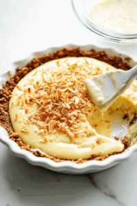 This image shows a luscious lemon filling being poured over a ginger cookie crust in a pie dish, forming the base for the vegan lemon pie before setting.