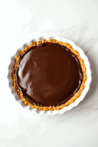 this image shows The creamy chocolate filling is poured into the baked crust, ready to set into a perfect pie layer.