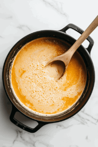 This image shows vegetable stock and creamy coconut cream being poured into the pot with vegetables, creating a rich and velvety texture for the soup.