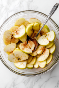 This image shows fresh apples being peeled, cored, and sliced, preparing them for the filling of a homemade vegan rustic apple pie.