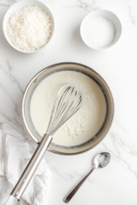 This image shows a rich and creamy coconut filling being whisked in a saucepan, with steam rising as it thickens into a luscious texture for the pie.