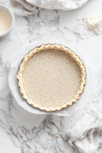 This image shows the tart crust lined with a sheet of baking parchment, weighted down with pie weights or beans to prevent puffing.