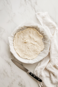This image shows the rolled-out dough being carefully placed into a pie dish, ready to be filled with the prepared apple mixture.