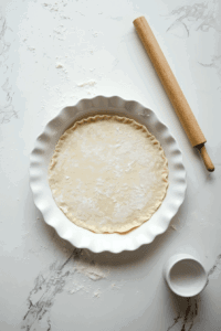 This image shows a pie pan lined with a rolled-out crust, edges trimmed and ready to be filled with the cherry mixture.