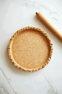 This image shows a pie pan being lined with a neatly rolled-out crust, edges crimped and ready to hold the sweet potato filling.