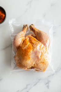 this image shows seasoned whole chicken is shown placed in a bowl and covered, resting in the refrigerator to allow the spices to penetrate for better flavor.