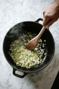 This image shows diced onion and celery being sautéed in a pot, releasing their aromatic flavors as the base for the vegan broccoli cheese soup.