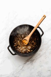 This image shows diced onion and minced garlic being sautéed in a skillet, releasing their aromatic flavors as the base for vegan broccoli cheese soup.