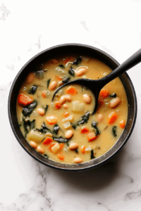 This image shows a steaming bowl of vegetable and pinto bean soup, garnished with fresh thyme leaves, ready to be enjoyed as a comforting meal.