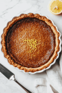 This image shows a slice of warm Vegan Treacle Tart being served with a scoop of vanilla ice cream, a perfect dessert to enjoy while still warm.