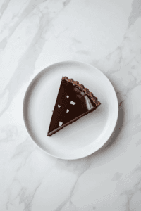 This image shows the vegan dark chocolate tart sliced and ready to serve, with its glossy chocolate filling and crisp crust creating a delectable dessert presentation.
