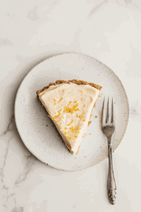 This image shows a creamy slice of vegan lemon pie being served, beautifully garnished with bright lemon zest, highlighting its tangy and refreshing flavor.