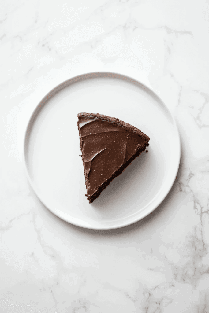 This image features a moist triangular slice of slow-cooked chocolate cake, topped with a smooth layer of chocolate.