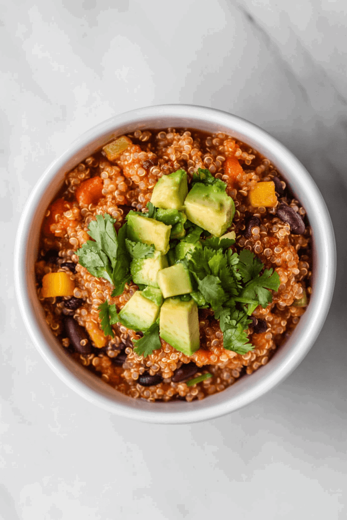 this image shows hearty bowl of slow-cooker quinoa chili, enriched with colorful vegetables, topped with avocado slices and fresh cilantro.