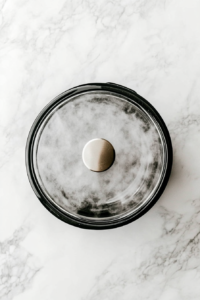 this image shows crockpot is shown cooking the whole chicken, surrounded by steam and onions, ensuring the meat turns tender and juicy.