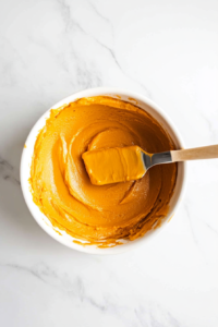 This image shows a spatula spreading the sweet potato filling evenly into the pre-made pie crust.