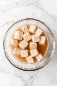 This image shows tofu nuggets being soaked in a flavorful broth to absorb spices and enhance their taste for Wendy's-style spicy chicken nuggets.