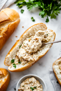 This image shows a generous layer of tangy remoulade sauce being spread on freshly sliced French rolls, adding flavor to the Po'Boy sandwich.