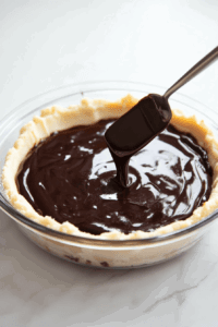 This image shows a spatula spreading a creamy or savory filling evenly over a pre-baked crust, ensuring a smooth and uniform layer for the dish.