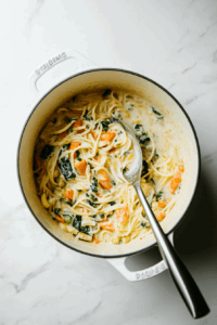 this image shows Freshly squeezed lemon juice being stirred into the pasta primavera, adding a bright and tangy flavor to the creamy vegan dish.