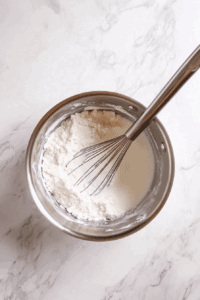 This image shows full-fat coconut milk being stirred into the sugar and cornstarch mixture, creating a creamy base for the Vegan Sugar Cream Pie filling.