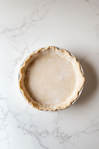 This image shows a pre-made pie crust thawing on a kitchen counter, ready to be filled with sweet potato and pecan layers.