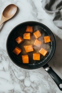 This image shows whole sweet potatoes boiling in a pot of water on the stovetop, softening them for the pie filling.