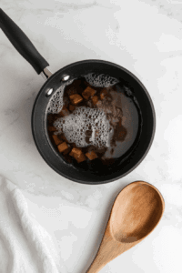 This image shows bright orange sweet potato cubes simmering in a saucepan filled with water, being cooked until tender.