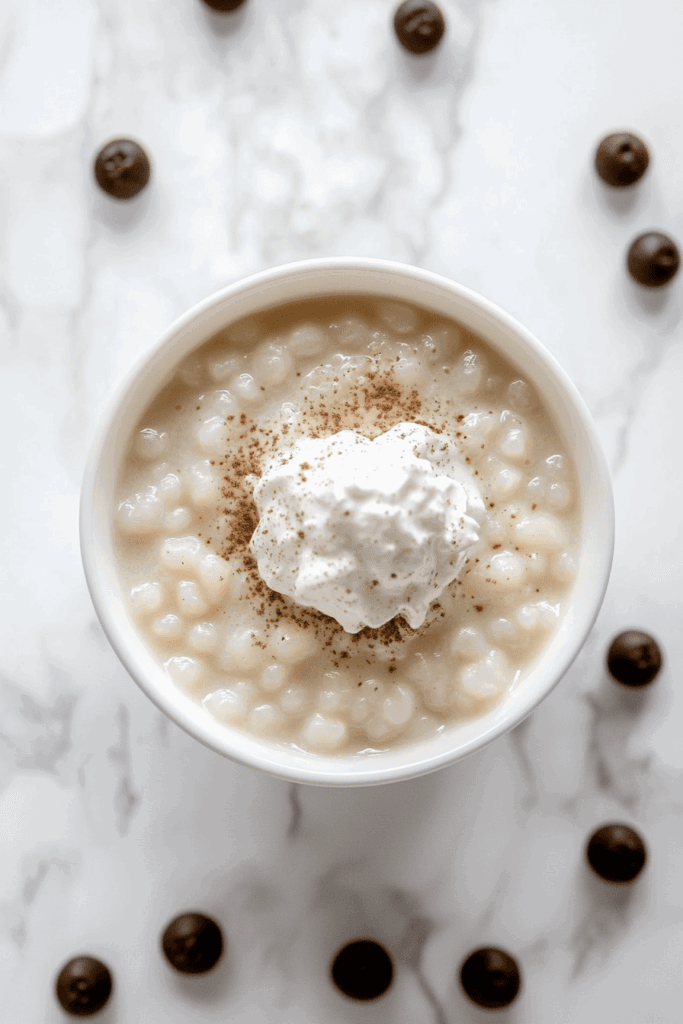 This image presents a delightful tapioca pudding, topped with a swirl of whipped cream and a dusting of cinnamon, served in a white bowl.