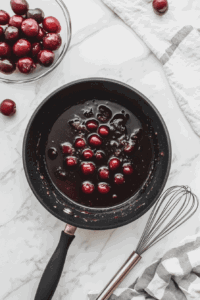 This image shows a bubbling saucepan with cherry juice being reduced to a thick and glossy consistency, ready to combine with whole cherries.