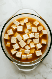 This image shows Bite-sized tofu pieces soaking in a spiced marinade, ensuring deep flavor absorption for a crispy tofu dish.