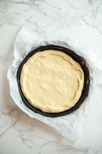 This image shows the shaped fathead dough being placed onto a round pizza pan lined with parchment paper, ready for baking.