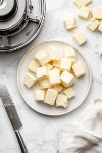 This image shows vegan butter being neatly cut into small cubes on a cutting board, ready to be incorporated into the pie crust mixture.