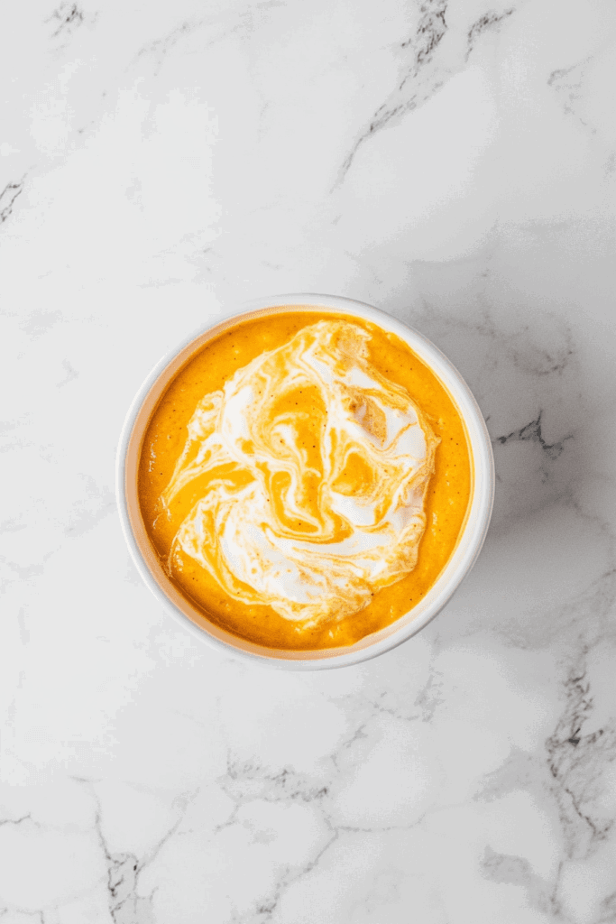 this image shows A velvety vegan butternut squash soup served with a swirl of creamy goodness in a white bowl.