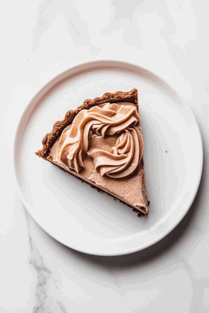 this image shows A light and airy slice of vegan chocolate peanut butter mousse pie, topped with a delicate swirl of mousse and served on a white round plate.