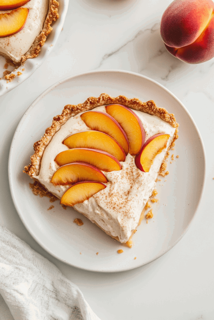 this image shows delightful vegan peach cream pie featuring a golden-brown crust, a creamy filling, and perfectly arranged fresh peach slices as a garnish.