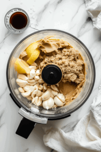 this image shows A bowl with peanut butter, soy sauce, lime juice, and spices being whisked into a creamy peanut sauce for Vegan Rainbow Peanut Noodles.