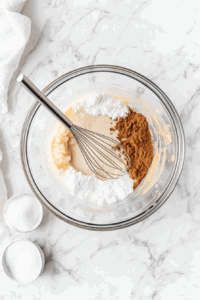 This image shows a bowl filled with pumpkin purée, brown sugar, and spices being whisked together to create a smooth and aromatic filling for the vegan pumpkin pie.