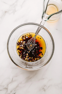 This image shows vinegar being gradually added to the olive oil and seasoning mixture while whisking, creating a smooth and flavorful Greek salad dressing.