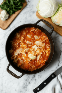 This image shows shredded cabbage in a pan being stirred with a wooden spoon, softening and absorbing the surrounding flavors for a perfectly tender and aromatic result.